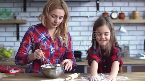 年轻的妈妈金发在盘子里混合小可爱的淘气女孩在厨房的桌子上玩面粉视频的预览图
