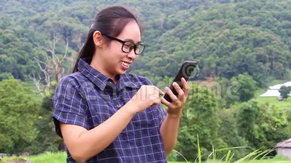亚洲年轻女性手持智能手机举起手臂在自然背景下看上去很成功视频的预览图