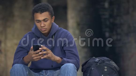 孤独的年轻人坐在街上听智能手机音乐青春期的不安全感视频的预览图