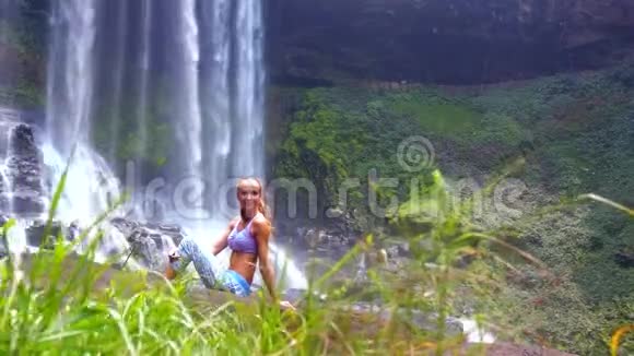 美丽的女孩坐在瀑布后面的草地上休息视频的预览图