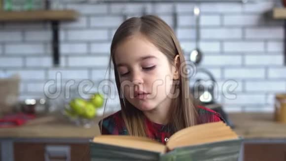 一个穿格子衬衫的漂亮小女孩坐在餐桌旁看书的画像视频的预览图