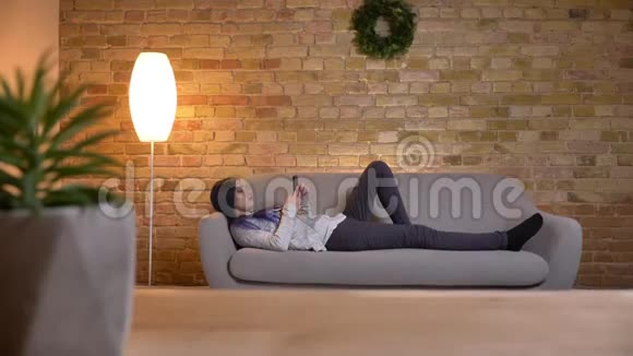 在舒适的家中躺在沙发上用手机拍摄的年轻有魅力的白种人潮女的特写镜头视频的预览图