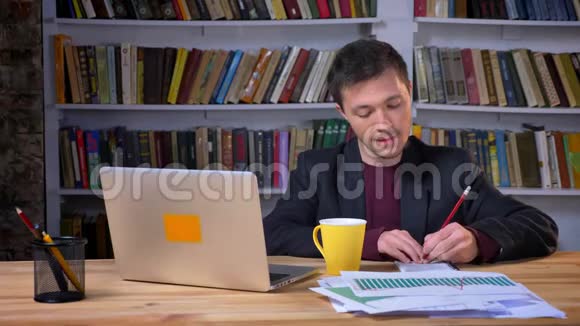 吸引人的成年商人在笔记本电脑旁边做笔记喝咖啡时面部表情愉快而满意视频的预览图