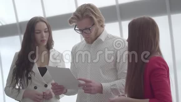 戴眼镜的金发男子向站在他两边的两位女同事解释了他的想法她穿着一件轻而舒适的衣服视频的预览图