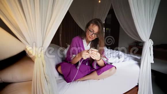 美丽的女人在床上使用手机管理智能连接的家庭移动应用程序视频的预览图