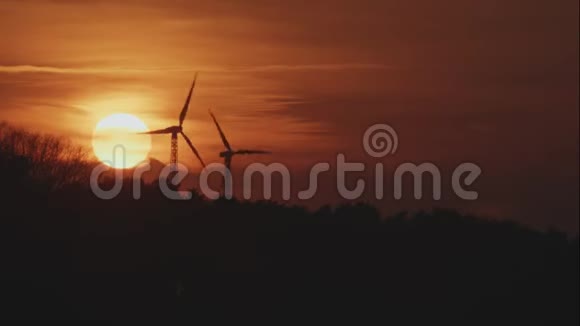 日落时分在森林后面有两个旋转风力涡轮机视频的预览图