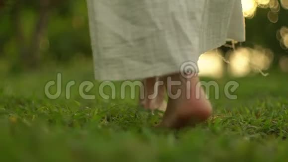 黎明时分穿着波霍式白色亚麻连衣裙的年轻女子赤脚走在年轻的草地上视频的预览图