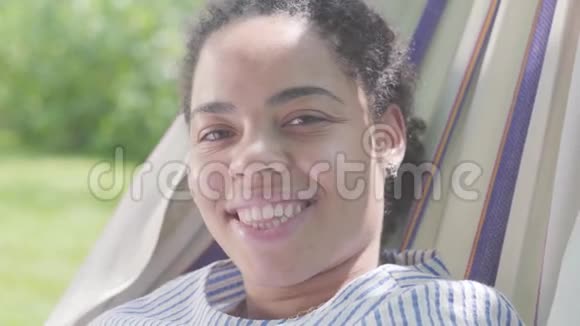 可爱快乐的非裔美国女人的特写脸躺在吊床上在花园里放松户外休闲视频的预览图