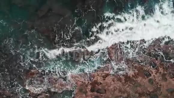 惊涛骇浪撞击岩石海滩的空中景色近距离无人驾驶飞机拍摄的海浪创造泡沫和飞溅在悬崖上视频的预览图