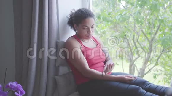可爱的非裔美国女人坐在窗台上用指甲锉剪指甲她关心自己视频的预览图