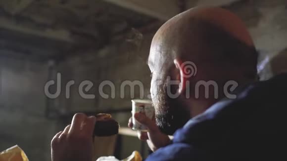 一个秃头留胡子的家伙正在用一次性杯子喝热饮还咬着一个面包视频的预览图