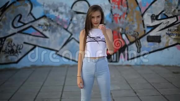 夏天晚上一个穿牛仔裤和t恤的女孩在大楼背景上的肖像街道视频的预览图