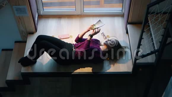 女人正在看一本书躺在窗边的楼梯上逃避现实视频的预览图