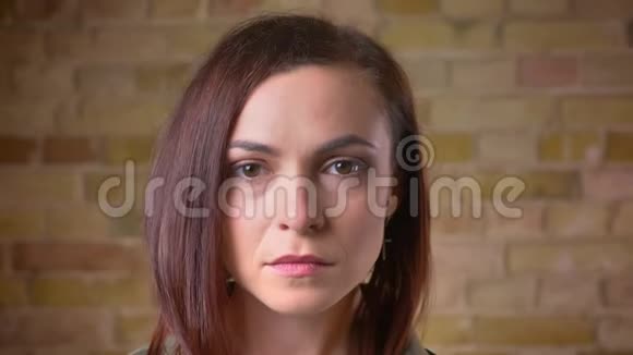 一个年轻美丽的棕色头发的女人在布里克肯墙背景上全神贯注地观看镜头视频的预览图