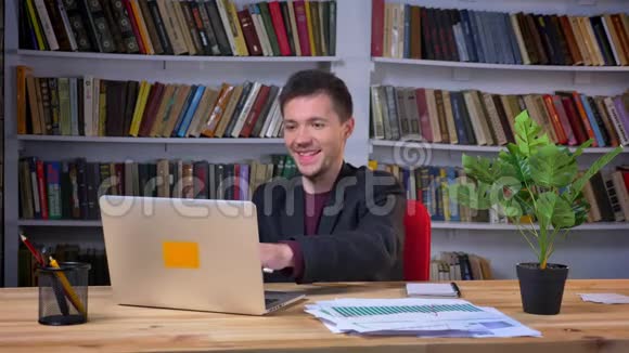 有魅力的成年商人坐在笔记本电脑前拿着书架在办公室里欢笑和快乐视频的预览图