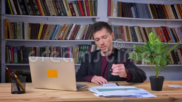 有魅力的男生在笔记本电脑上工作带书架在图书馆做笔记视频的预览图