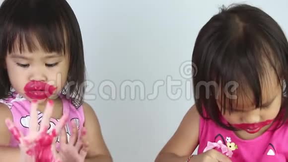 亚洲小女孩在白色背景上为妹妹涂红色口红视频的预览图