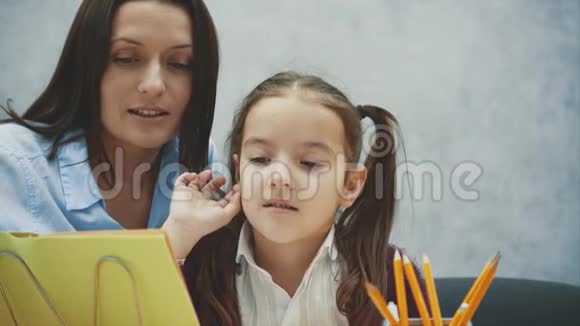 妈妈和女儿坐在灰色背景的桌子旁在阅读过程中书籍微笑拥抱概念视频的预览图