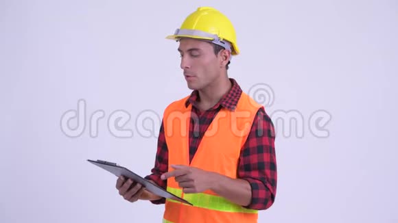 年轻快乐的西班牙裔建筑工人一边在剪贴板上看书一边说话视频的预览图