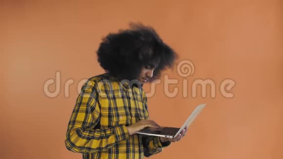 非裔美国人在笔记本电脑上打字在橙色背景上微笑情感概念视频的预览图