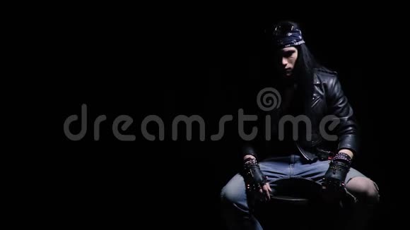 年轻的摇滚歌手黑发交叉双腿在演播室摆姿势轻微的慢动作视频的预览图