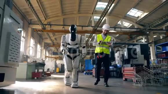 男工程师和一个机器人正沿着工厂行走视频的预览图