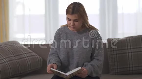 坐在家里沙发上的胖女孩看书胖女人手里拿着书休闲智能加码女士视频的预览图