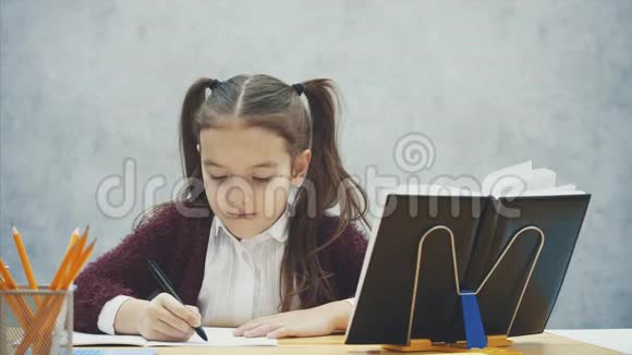 在灰色背景下关闭聪明的女学生在这段时间里他坐在桌子旁仔细写作业视频的预览图