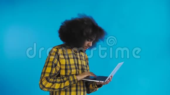 非裔美国人在笔记本电脑上打字在蓝色背景上微笑情感概念视频的预览图