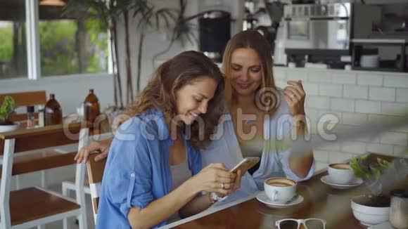 两个女人慢动作在咖啡馆里用智能手机分享咖啡视频的预览图
