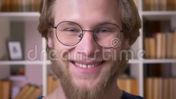 在学校图书馆里戴着眼镜笑着看着摄像机的成年男学生的特写镜头视频的预览图