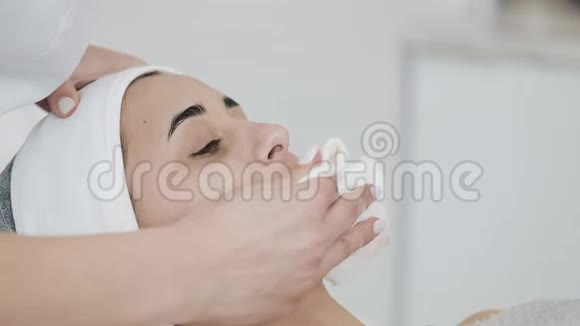 美丽的女人在水疗沙龙按摩她的脸之前用餐巾擦拭她的脸慢动作视频的预览图