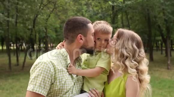 可爱的父母在夏天的公园里亲吻他们的儿子视频的预览图