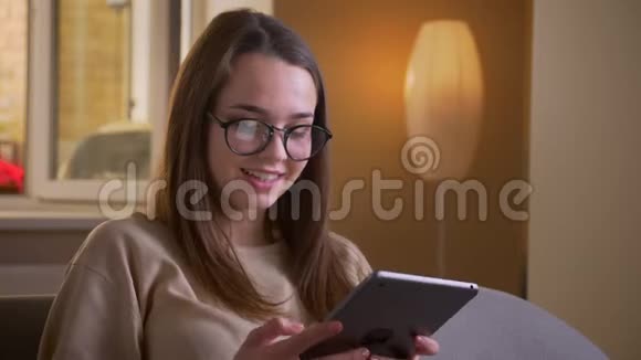 戴眼镜的年轻白种人女性的特写肖像使用平板电脑坐在室内沙发上视频的预览图