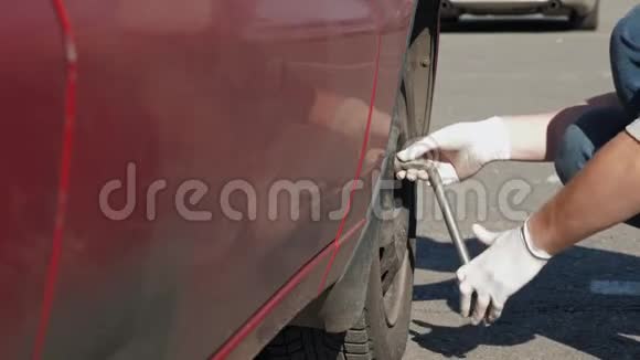 一个没有经验的戴白手套的人正试图在他那辆破破烂烂的红色汽车上拧开一个轮子视频的预览图