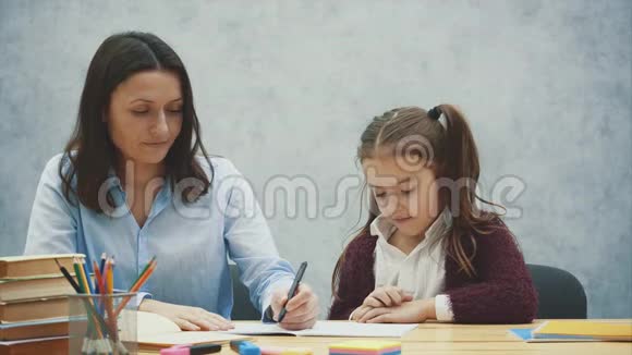 妈妈和女儿的灰色背景在这期间她为一个微笑的女儿写作业关系概念视频的预览图
