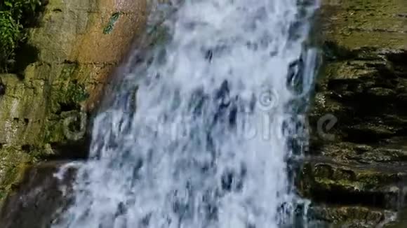 特写自然瀑布水流过生长着绿色苔藓的石头缓慢流动视频的预览图