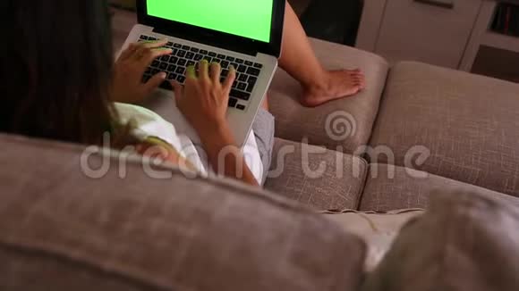 一个年轻的女人在她的笔记本电脑上工作家里的绿色屏幕坐在客厅的沙发上视频的预览图