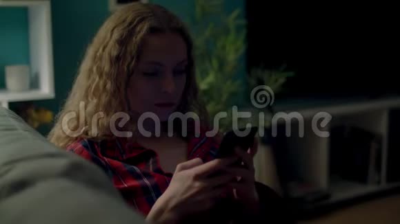 晚上在沙发上使用智能手机的女士手持镜头视频的预览图