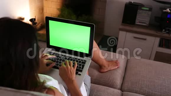 一个年轻的女人在她的笔记本电脑上工作家里的绿色屏幕坐在客厅的沙发上视频的预览图
