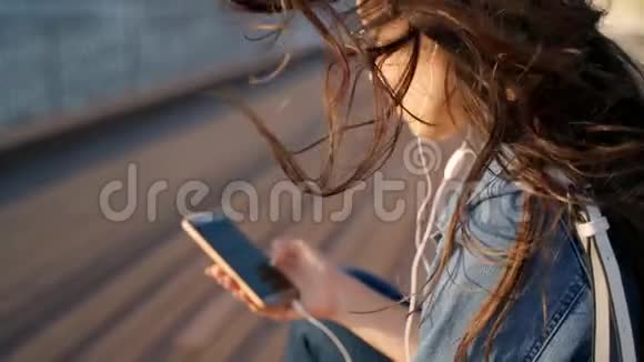 一个戴眼镜的年轻女孩坐在街上用耳机听音乐手里拿着电话的女孩视频的预览图