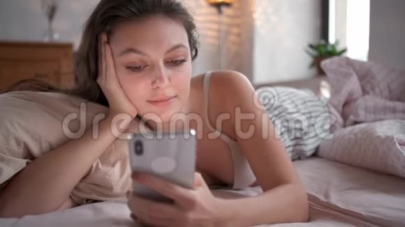 在家放松的女人在她明亮的卧室里读短信在床上用智能手机查看社交应用视频的预览图