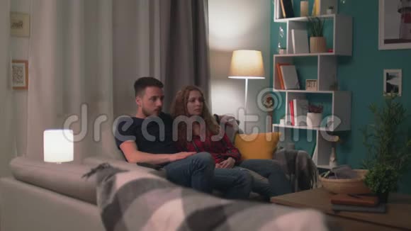 一对年轻夫妇深夜躺在沙发上观看恐怖片视频的预览图