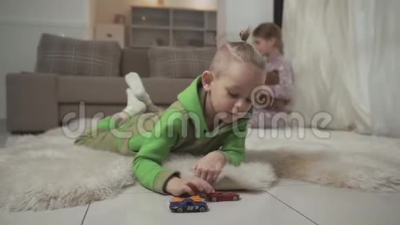 有时髦发型的小男孩和他的玩具车躺在毛茸茸的地毯上姐姐在玩泰迪视频的预览图