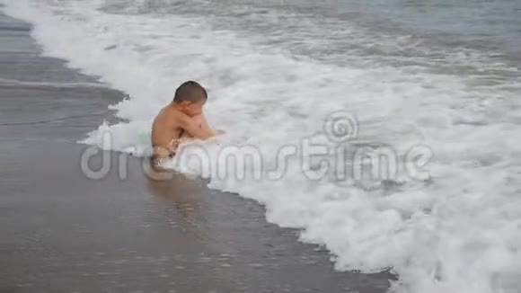 男孩坐在波浪里用头遮住孩子的波浪慢动作视频的预览图