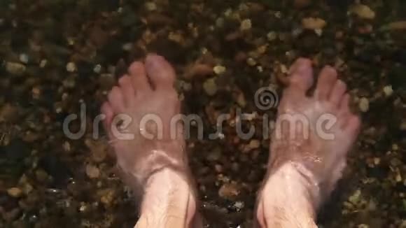 一个赤脚的人站在水中的鹅卵石海岸上水给他洗了脚并制定了应对计划视频的预览图