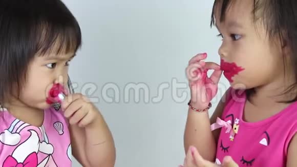 亚洲小女孩在嘴唇上涂红色口红为白色背景的妹妹涂红色口红视频的预览图