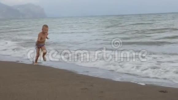晒黑的男孩在金色的沙滩上沿着海岸奔跑慢动作视频的预览图