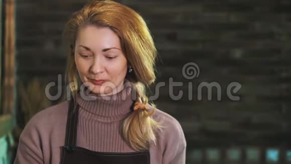 一个穿着围裙的女花匠站在一家花店的柜台后面看着镜头微笑着视频的预览图