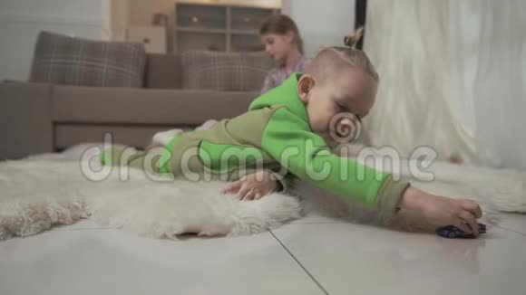 有时髦发型的小男孩和他的玩具车躺在毛茸茸的地毯上姐姐在玩泰迪视频的预览图